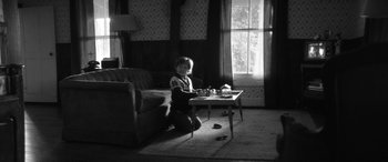 Movie still from “The Eyes of My Mother” (2016), directed by Nicolas Pesce – A child sitting on the floor in front of a coffee table; Wide shot, High angle