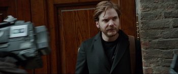 Movie still from “The Face of an Angel” (2014), directed by Michael Winterbottom – A man in a black jacket is standing in front of a wooden door; Close Up shot, Over the shoulder angle