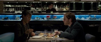 Movie still from “The Face of an Angel” (2014), directed by Michael Winterbottom – Two men sitting at a table in front of a fish tank; Medium shot, Over the shoulder angle