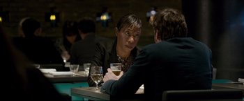 Movie still from “The Face of an Angel” (2014), directed by Michael Winterbottom – A woman sitting at a table with a glass of white wine; Medium shot, Over the shoulder angle