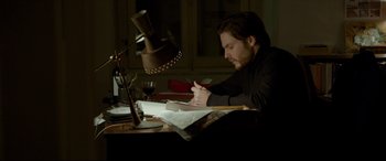 Movie still from “The Face of an Angel” (2014), directed by Michael Winterbottom – A man sitting at a desk writing on a piece of paper; Medium shot, High angle