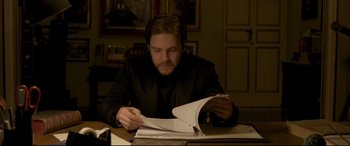 Movie still from “The Face of an Angel” (2014), directed by Michael Winterbottom – A man sitting at a table looking at papers; Medium shot, Over the shoulder angle