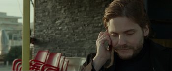 Movie still from “The Face of an Angel” (2014), directed by Michael Winterbottom – A man sitting at a table talking on a cell phone; Close Up shot, High angle