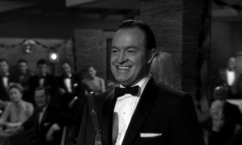 Movie still from “The Facts of Life” (1960), directed by Melvin Frank – A man in a suit and bow tie holding a wine glass; Close Up shot, Over the shoulder angle