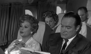 Movie still from “The Facts of Life” (1960), directed by Melvin Frank – An old black and white photo of a man and two women on an airplane; Medium shot, High angle