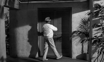 Movie still from “The Facts of Life” (1960), directed by Melvin Frank – A black and white photo of a man walking in front of a door; Wide shot, High angle