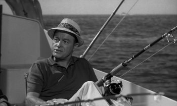 Movie still from “The Facts of Life” (1960), directed by Melvin Frank – A black and white photo of a man sitting on a sailboat; Medium shot, High angle