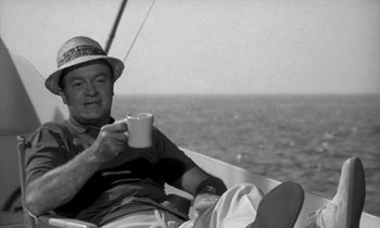 Movie still from “The Facts of Life” (1960), directed by Melvin Frank – A black and white photo of a man drinking a cup of coffee on a sailboat; Medium shot, High angle