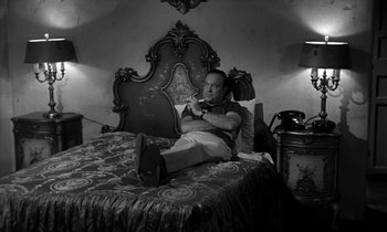 Movie still from “The Facts of Life” (1960), directed by Melvin Frank – A black and white photo of a man sitting on a bed; Medium shot, High angle
