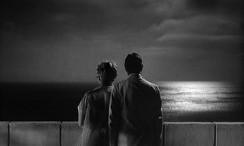 Movie still from “The Facts of Life” (1960), directed by Melvin Frank – A man and a woman standing next to each other near the ocean; Medium shot, High angle