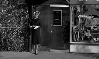 Movie still from “The Facts of Life” (1960), directed by Melvin Frank – A black and white photo of a woman standing in front of a building; Wide shot, Low angle