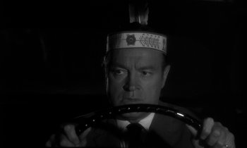 Movie still from “The Facts of Life” (1960), directed by Melvin Frank – A black and white photo of a man in a suit holding a steering wheel; Close Up shot, Over the shoulder angle