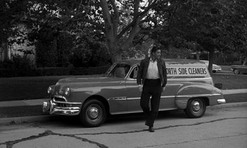 Movie still from “The Facts of Life” (1960), directed by Melvin Frank – A man walking next to an old car on the side of the road; Wide shot, High angle