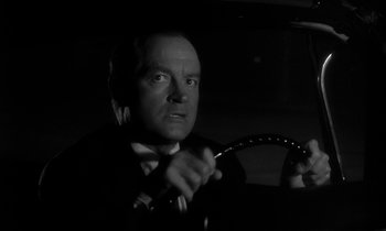 Movie still from “The Facts of Life” (1960), directed by Melvin Frank – A black and white photo of a man holding a steering wheel; Close Up shot, Low angle