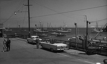Movie still from “The Facts of Life” (1960), directed by Melvin Frank – An old car parked on the side of the road near the water; Extreme Wide shot, High angle