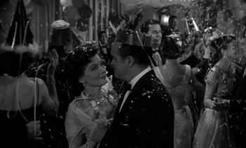 Movie still from “The Facts of Life” (1960), directed by Melvin Frank – A man and a woman kissing in front of a group of people; Medium shot, High angle