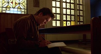 Movie still from “The Falcon and the Snowman” (1985), directed by John Schlesinger – A man sitting on a bench writing in a notebook; Medium shot, Low angle