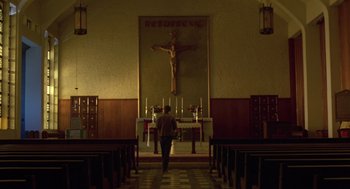 Movie still from “The Falcon and the Snowman” (1985), directed by John Schlesinger – A person standing in front of a cross in a church; Extreme Wide shot, Low angle
