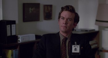 Movie still from “The Falcon and the Snowman” (1985), directed by John Schlesinger – A man in a suit and tie sitting in a room; Close Up shot, Over the shoulder angle