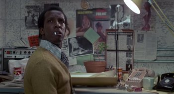 Movie still from “The Falcon and the Snowman” (1985), directed by John Schlesinger – A man standing in front of a wall with posters on the wall behind him; Close Up shot, Low angle