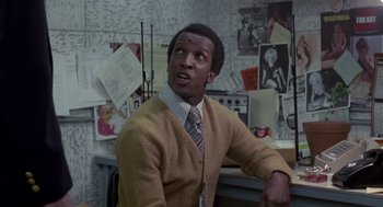 Movie still from “The Falcon and the Snowman” (1985), directed by John Schlesinger – A man wearing a sweater and a tie in a room; Medium shot, Low angle