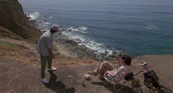 Movie still from “The Falcon and the Snowman” (1985), directed by John Schlesinger – A man standing next to a woman sitting on a lawn chair; Wide shot, High angle