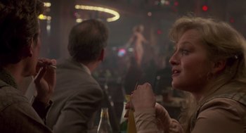 Movie still from “The Falcon and the Snowman” (1985), directed by John Schlesinger – Two people sitting at a table in front of a crowd; Close Up shot, Over the shoulder angle