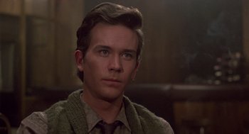 Movie still from “The Falcon and the Snowman” (1985), directed by John Schlesinger – A man with a sweater and a tie on; Close Up shot, Over the shoulder angle