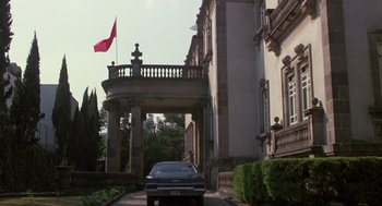 Movie still from “The Falcon and the Snowman” (1985), directed by John Schlesinger – A car parked in front of a building with a red flag on top of it; Extreme Wide shot, Low angle