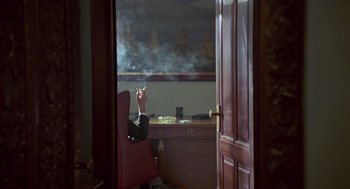 Movie still from “The Falcon and the Snowman” (1985), directed by John Schlesinger – A person sitting in a chair with a cigarette in their hand; Wide shot, High angle