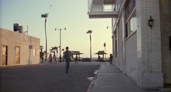 Movie still from “The Falcon and the Snowman” (1985), directed by John Schlesinger – A man walking down a sidewalk next to palm trees; Extreme Wide shot, Low angle
