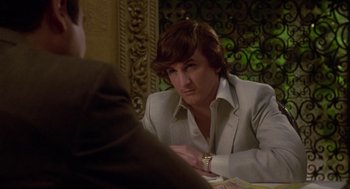 Movie still from “The Falcon and the Snowman” (1985), directed by John Schlesinger – A man sitting at a table with a watch in his hand; Medium shot, Over the shoulder angle