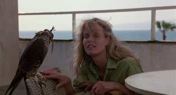 Movie still from “The Falcon and the Snowman” (1985), directed by John Schlesinger – A woman sitting next to a bird on top of a table; Close Up shot, Low angle