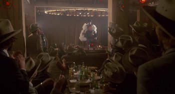 Movie still from “The Falcon and the Snowman” (1985), directed by John Schlesinger – A group of people sitting at a table with hats on; Wide shot, Over the shoulder angle