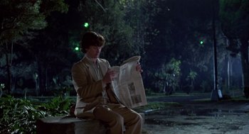 Movie still from “The Falcon and the Snowman” (1985), directed by John Schlesinger – A man sitting on top of a bench reading a newspaper; Wide shot, Over the shoulder angle