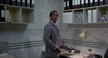 Movie still from “The Falcon and the Snowman” (1985), directed by John Schlesinger – A man in a gray suit holding a pair of shoes; Medium shot, Low angle