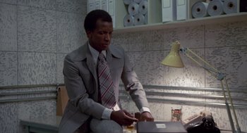 Movie still from “The Falcon and the Snowman” (1985), directed by John Schlesinger – A man in a gray suit and a red and white striped neck tie; Medium shot, Low angle