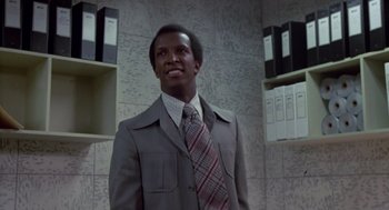 Movie still from “The Falcon and the Snowman” (1985), directed by John Schlesinger – A man in a suit and tie standing in front of a wall; Medium shot, Low angle