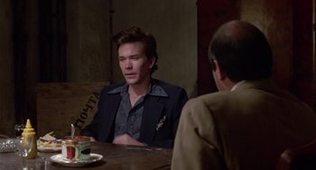 Movie still from “The Falcon and the Snowman” (1985), directed by John Schlesinger – A man sitting at a table with another man in front of him; Medium shot, Over the shoulder angle