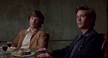 Movie still from “The Falcon and the Snowman” (1985), directed by John Schlesinger – Two people sitting at a table with a plate of food; Medium shot, Low angle