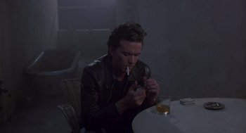 Movie still from “The Falcon and the Snowman” (1985), directed by John Schlesinger – A man sitting at a table with a cigarette in his mouth; Medium shot, High angle
