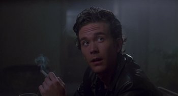 Movie still from “The Falcon and the Snowman” (1985), directed by John Schlesinger – A man smoking a cigarette while sitting on the ground; Close Up shot, Low angle