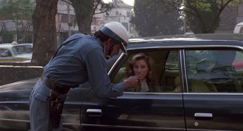 Movie still from “The Falcon and the Snowman” (1985), directed by John Schlesinger – A police officer taking a woman's cigarette out of a car window; Medium shot, Over the shoulder angle