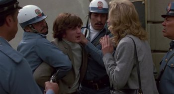 Movie still from “The Falcon and the Snowman” (1985), directed by John Schlesinger – A group of people standing next to each other on a street; Medium shot, Over the shoulder angle