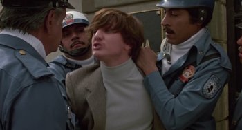 Movie still from “The Falcon and the Snowman” (1985), directed by John Schlesinger – A man in a suit is being held down by two police officers; Medium shot, Low angle