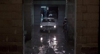 Movie still from “The Falcon and the Snowman” (1985), directed by John Schlesinger – A man standing in a garage with a car parked in it; Extreme Wide shot, High angle