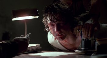 Movie still from “The Falcon and the Snowman” (1985), directed by John Schlesinger – A man with blood all over his face is looking at a lamp; Close Up shot, Low angle