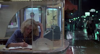 Movie still from “The Falcon and the Snowman” (1985), directed by John Schlesinger – A woman sitting at a table in a glass case; Medium shot, High angle