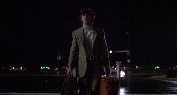 Movie still from “The Falcon and the Snowman” (1985), directed by John Schlesinger – A man in a suit carrying two suitcases at night; Medium shot, Low angle