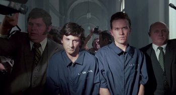 Movie still from “The Falcon and the Snowman” (1985), directed by John Schlesinger – A group of men standing next to each other in a room; Medium shot, Low angle